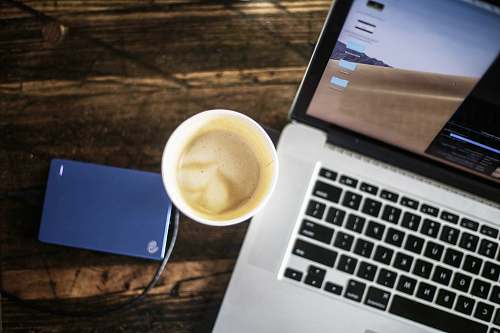 computer hardware cup of coffee latte between turned-on laptop and Seagate portable drive computer keyboard